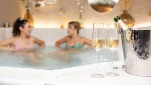 Un ambiente de spa con un jacuzzi, dos copas de vino blanco y una botella de champán en un cubo de metal.