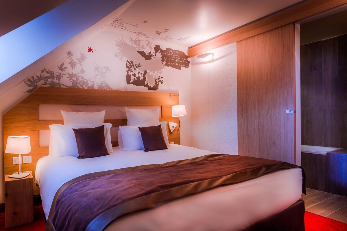 A modern hotel room with a large bed, wooden headboard, and a skylight.