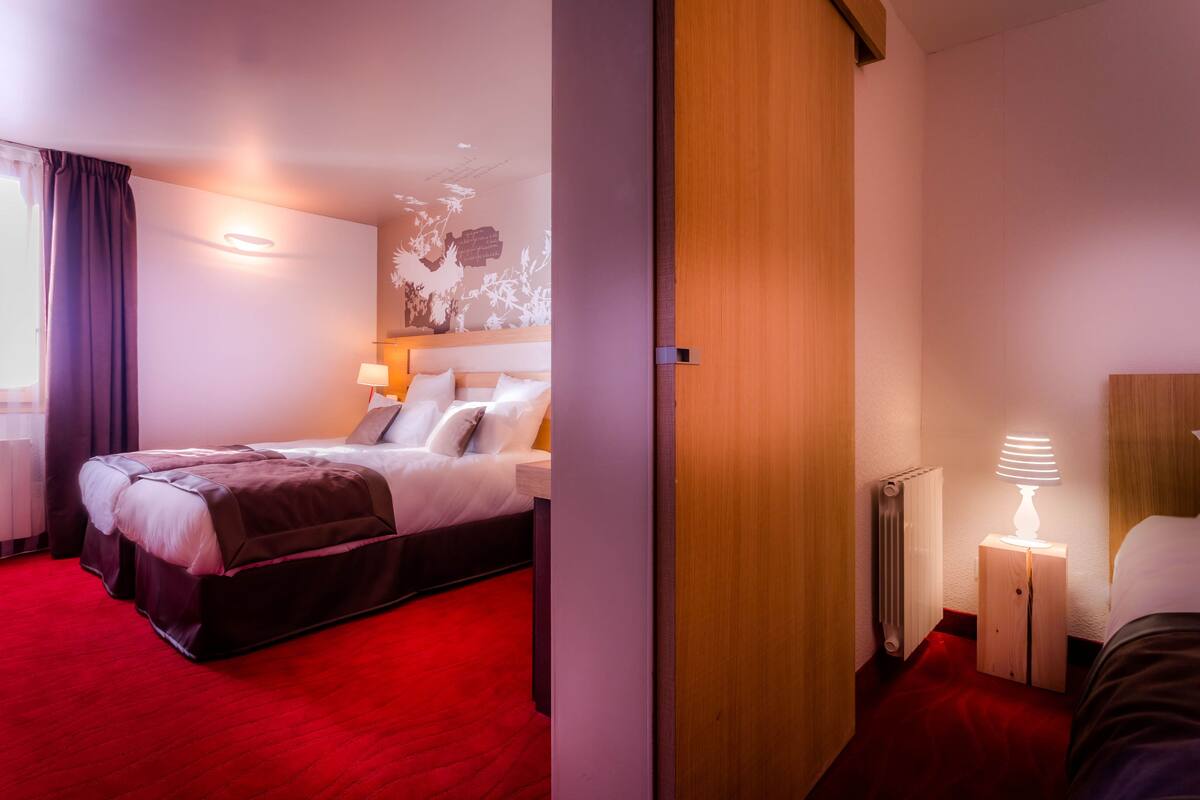 A hotel room with a large bed, a wooden headboard, a red carpet, a wall-mounted lamp, and a radiator.