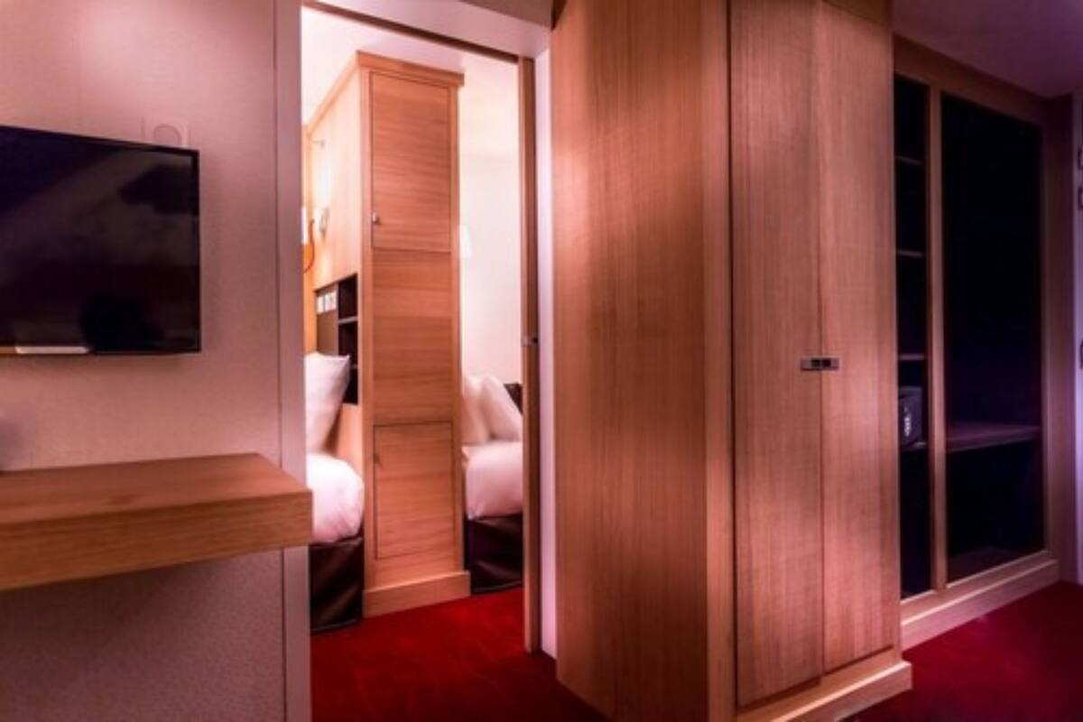 A hotel room with a wooden wardrobe, a television mounted on the wall, and a red carpet.