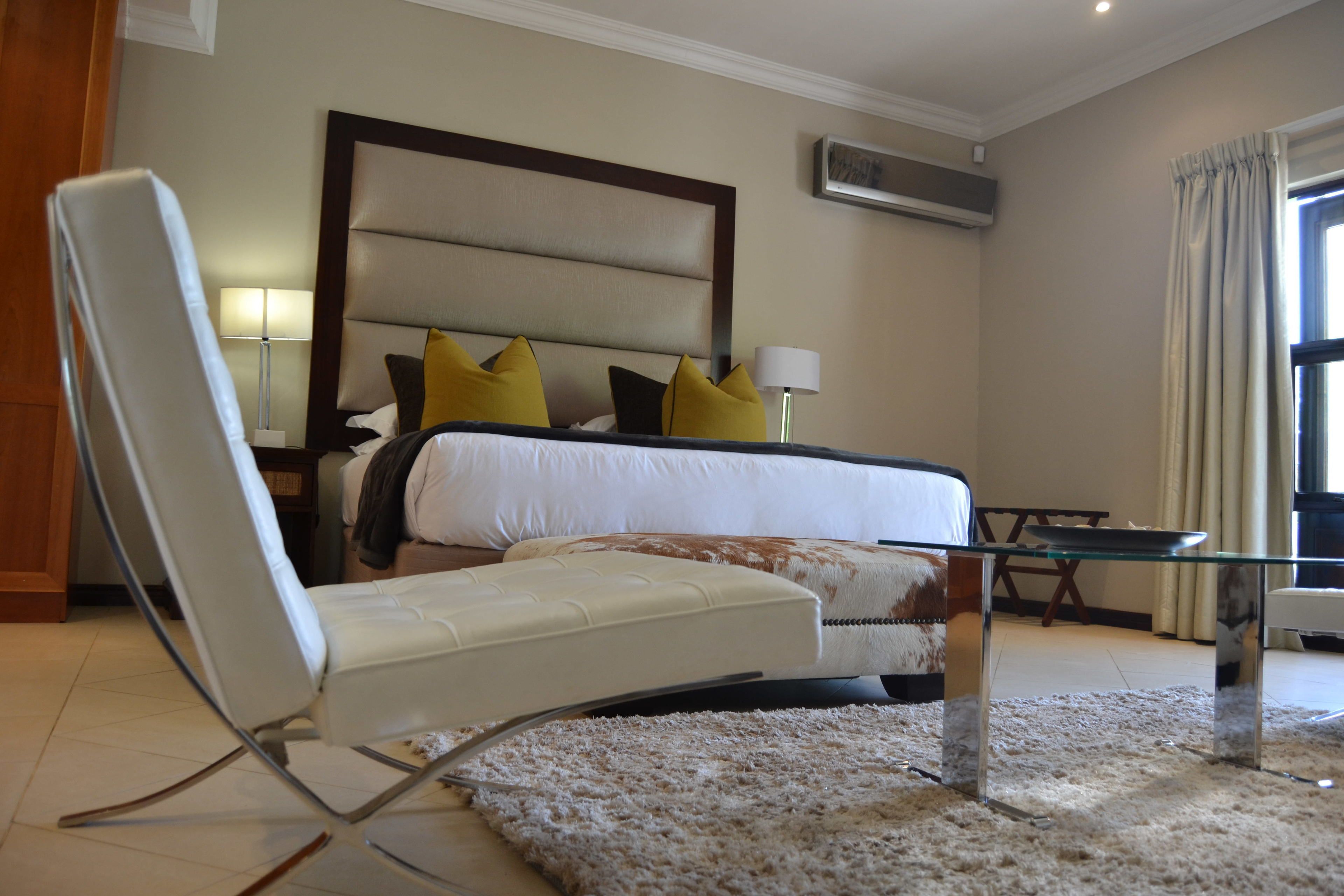 A modern hotel room with a large bed, a sitting area with a chair, a small table, and a large window with curtains.