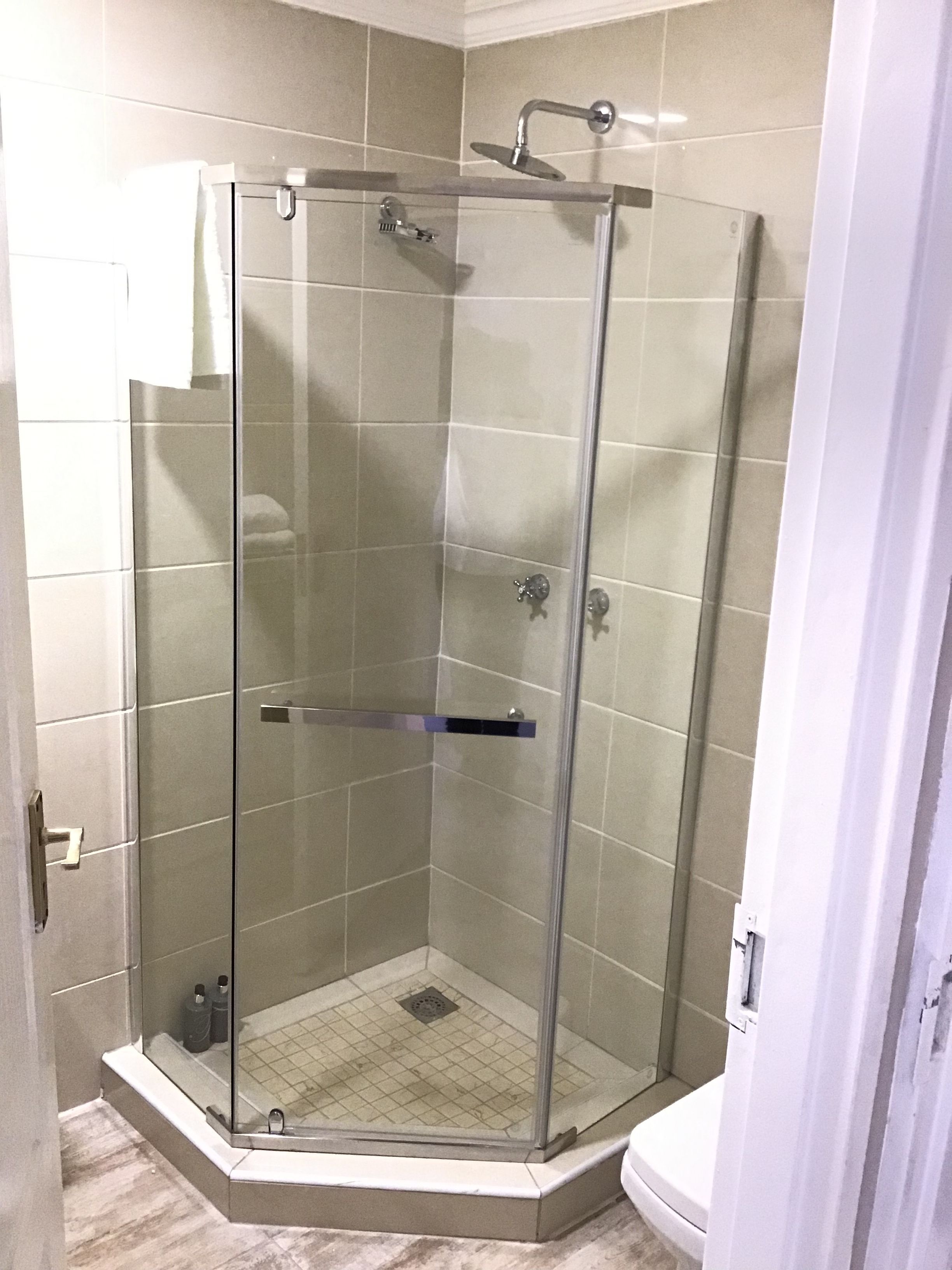 A glass-enclosed shower stall with a handheld showerhead, a handheld showerhead, and a handheld showerhead.