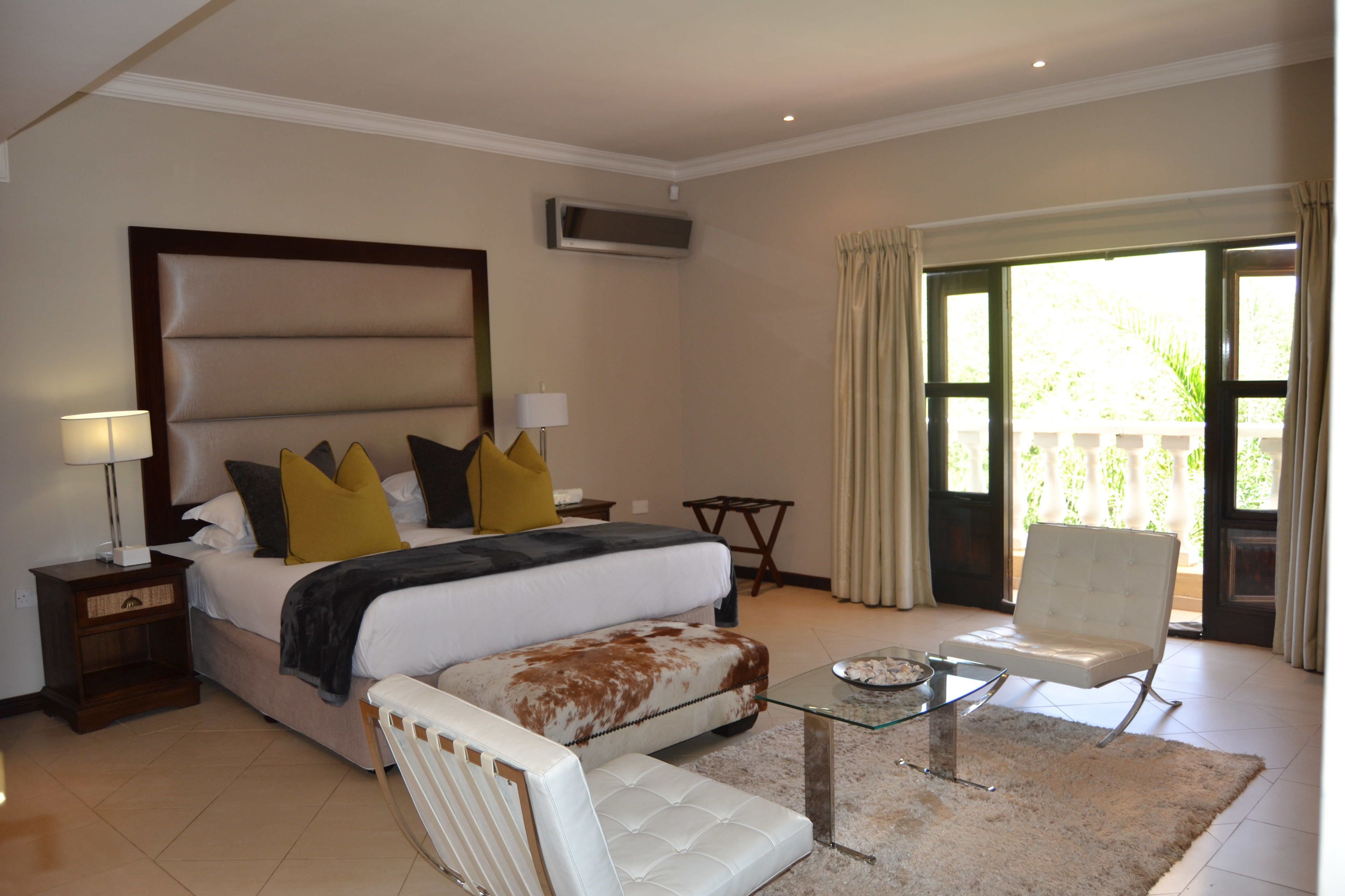 Habitación de hotel con una cama grande, un área de descanso con una mesa de vidrio, una silla y vistas al exterior.