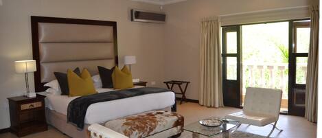 Habitación de hotel con una cama grande, un área de descanso con una mesa de vidrio, una silla y vistas al exterior.