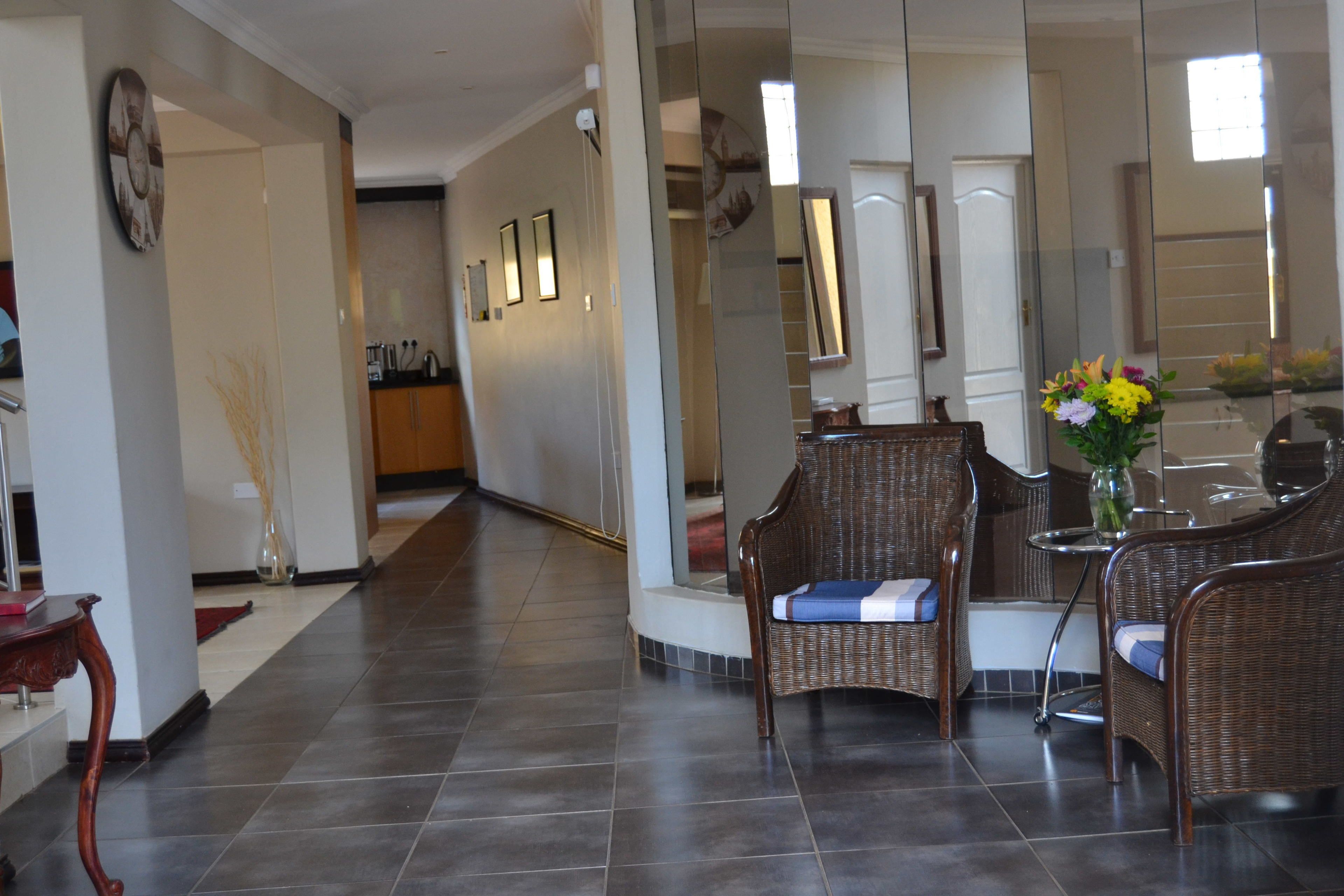 A spacious living area with a dining table and wicker chairs, a vase with flowers, and a large mirror reflecting the room.