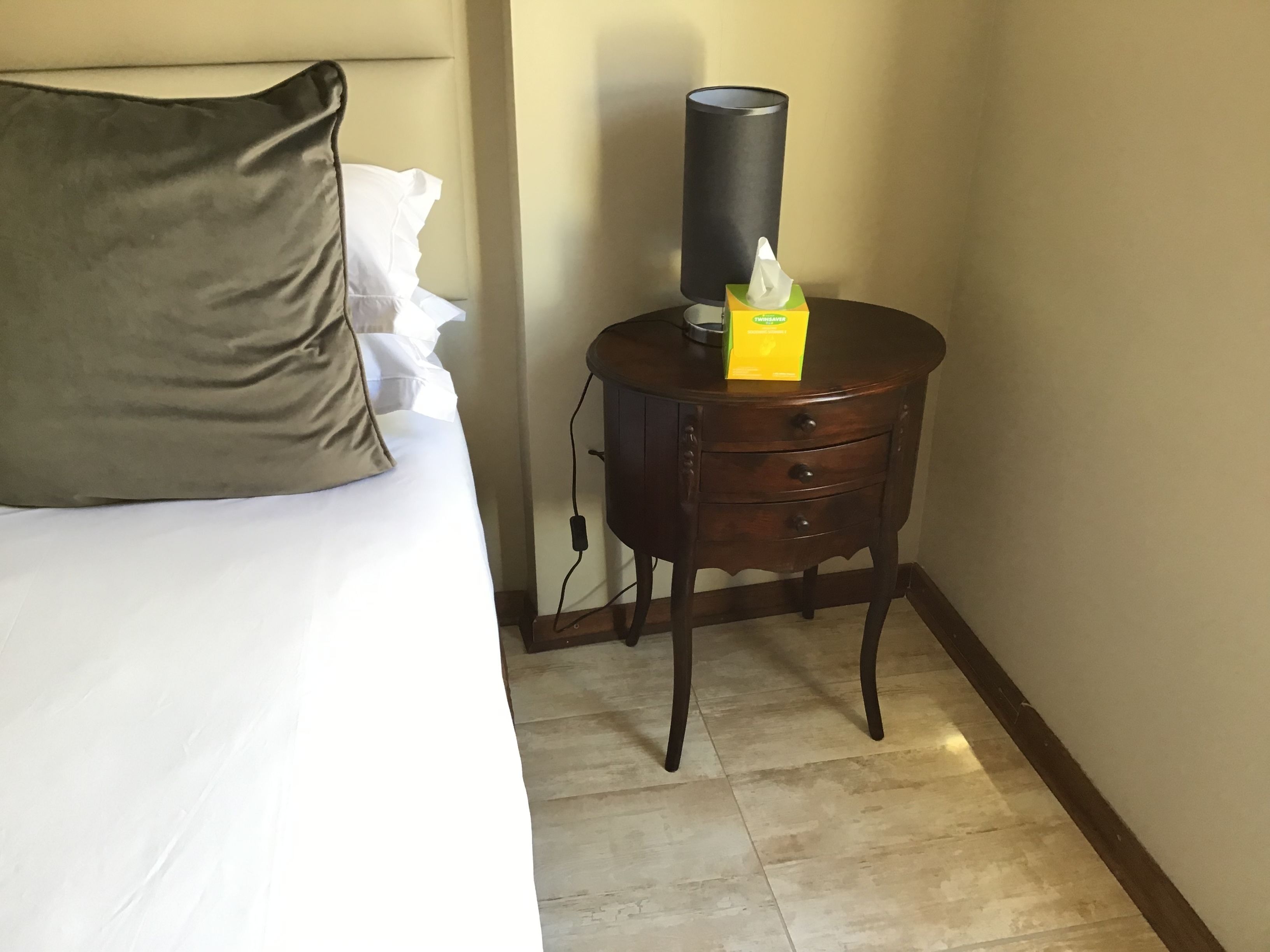 A hotel room with a bed, a bedside table with a lamp, and a tissue box.