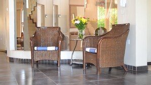 A lobby area with wicker chairs, a glass table, and a vase of flowers. - The Capital Guesthouse (Gaborone)