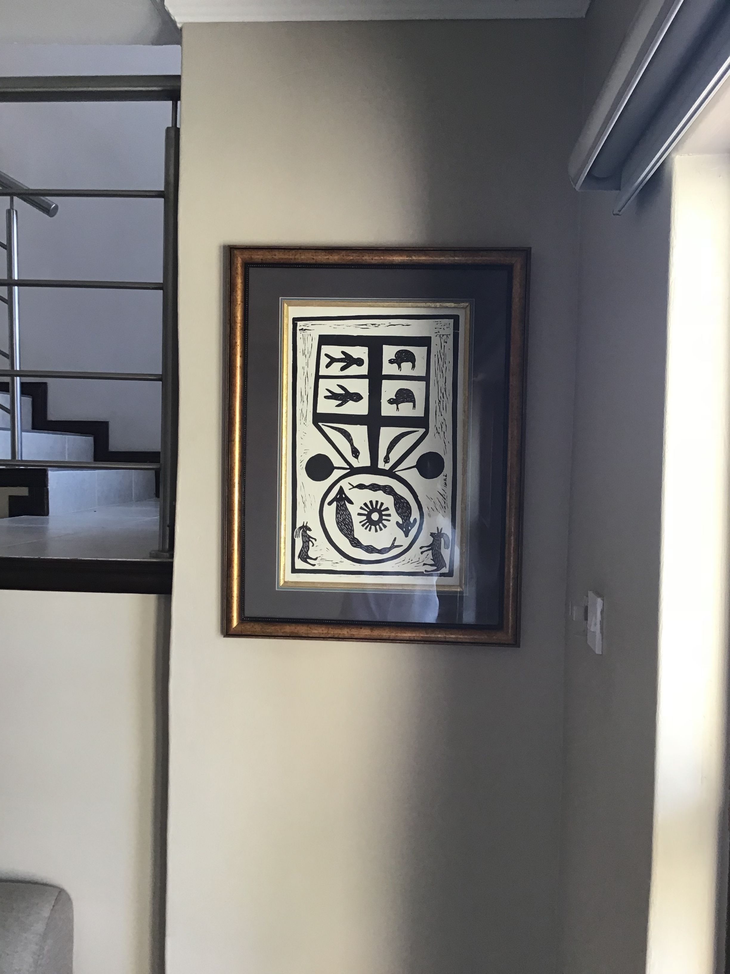 Ein gerahmtes Kunstwerk an einer Wand in einem Raum, im Hintergrund eine Treppe.