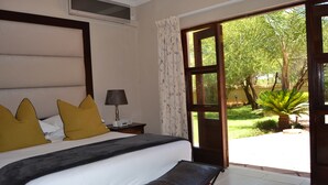 A bedroom with a bed, a nightstand, a lamp, and a view of the outdoors. - The Capital Guesthouse (Gaborone)