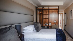 A hotel room with a large bed, a bedside table, a wardrobe, and a mirror. - The Capital Guesthouse (Gaborone)