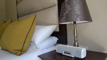 A neatly made bed with white and mustard pillows, a bedside table with a lamp, and a white electronic device on the table.
