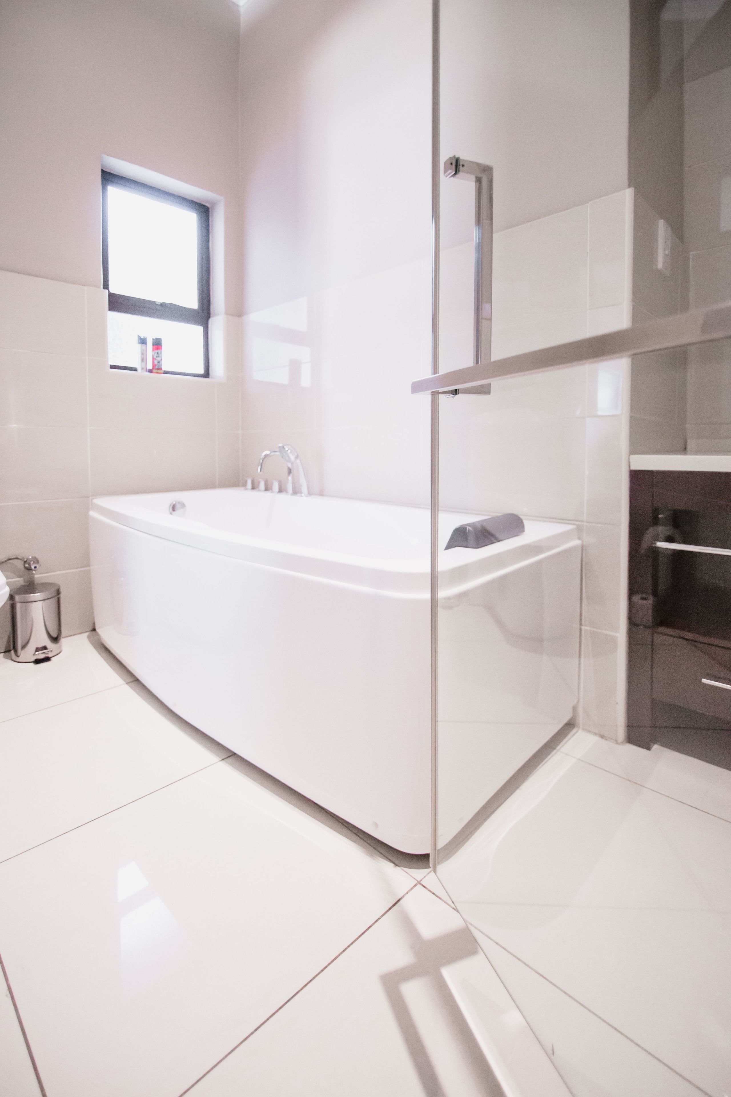 A modern bathroom with a freestanding bathtub, a glass shower enclosure, and a small window providing natural light.