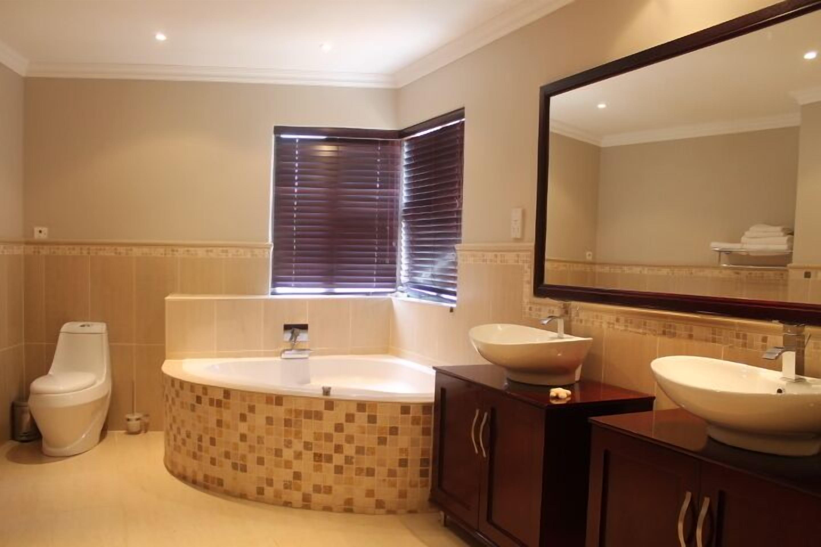 Une salle de bain avec une baignoire, deux lavabos, des toilettes et un grand miroir.
