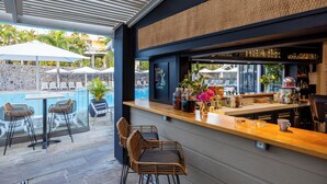 Un espace bar extérieur avec des chaises en osier, une piscine et des parasols.