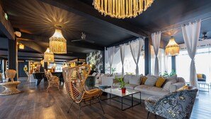 Un espace de détente moderne comprenant une table de billard, des fauteuils en osier, un ensemble de canapés et des lampes suspendues.