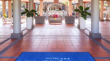 Entrada de hotel con felpudo azul que dice "HOTEL CREOLES", zona de bar con mostrador y disposición de asientos.