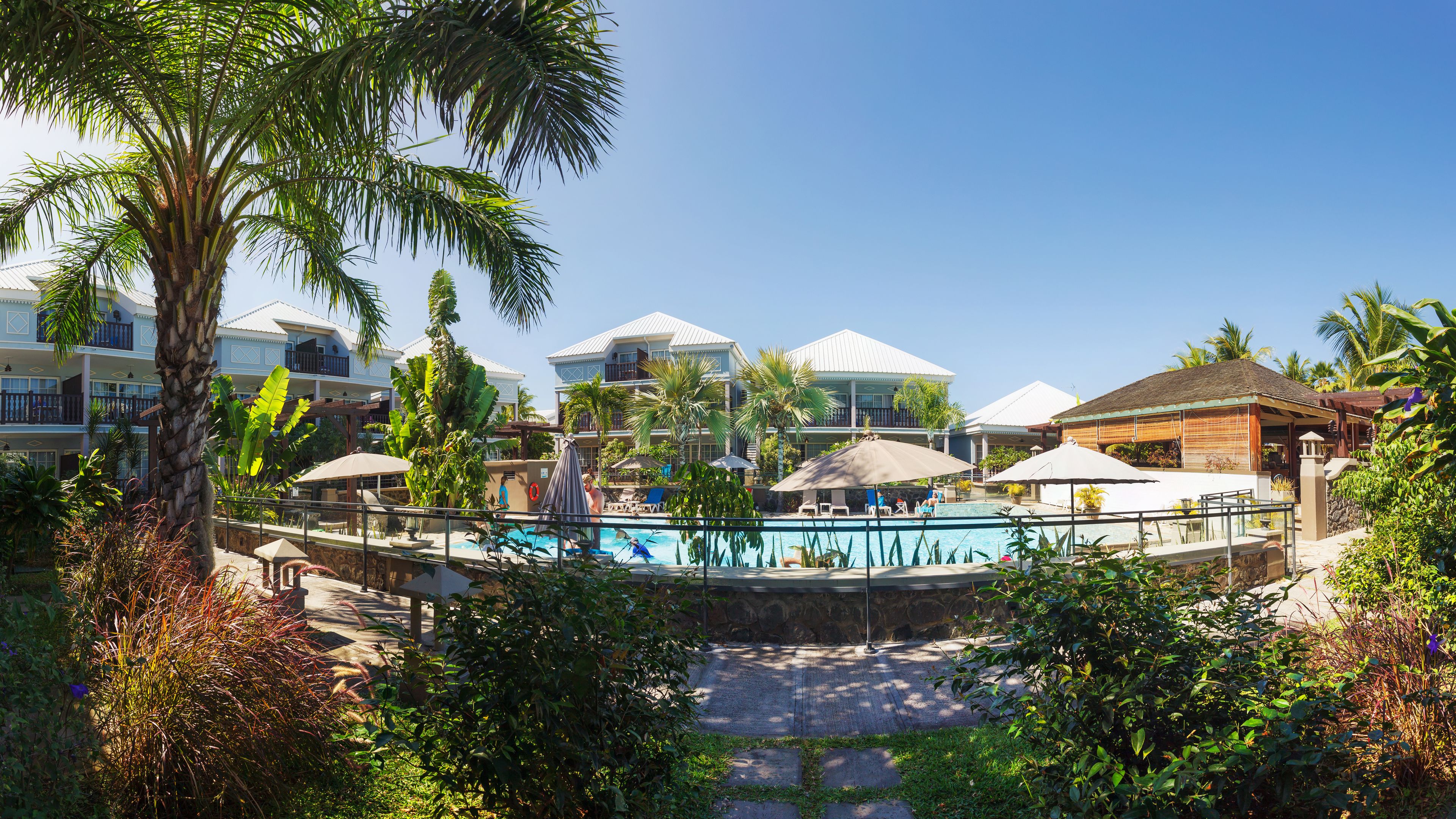 Un resort con piscina rodeada de palmeras y un camino de piedra.