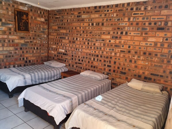 A room with two single beds, a brick wall, and a small wooden nightstand between them. - Limpopo Lodge (Polokwane)