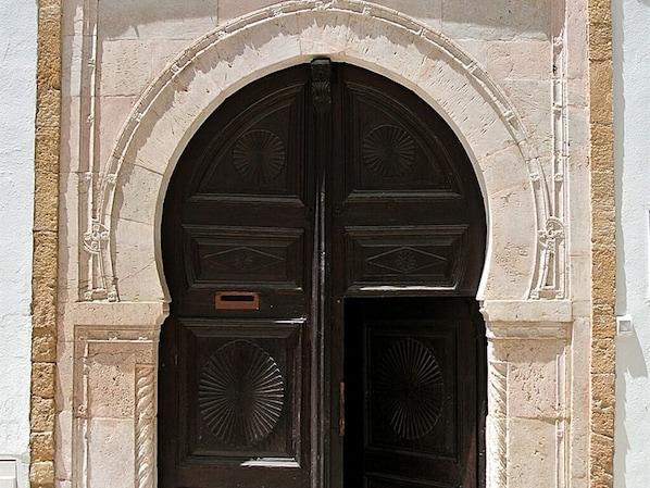 Uma porta dupla de madeira com esculturas detalhadas, emoldurada por um arco de pedra.