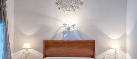 Un dormitorio con cama de madera, dos mesitas de noche con lámparas, un medallón decorativo en el techo y un aplique de pared.