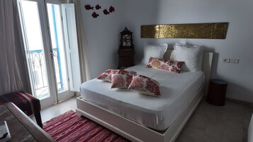 Une chambre à coucher avec un lit, des oreillers, une table de chevet, une horloge et une fenêtre.