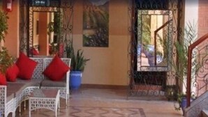 A covered outdoor seating area with a sofa and chairs, potted plants, and a metal gate. - Hotel Alkabir (Marrakech)