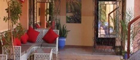 A covered outdoor seating area with a sofa and chairs, potted plants, and a metal gate.