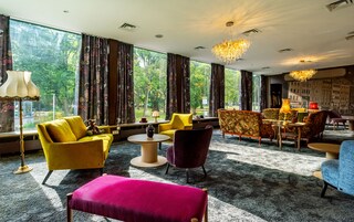 A modern hotel room with large windows, a dining area, and a variety of seating options.