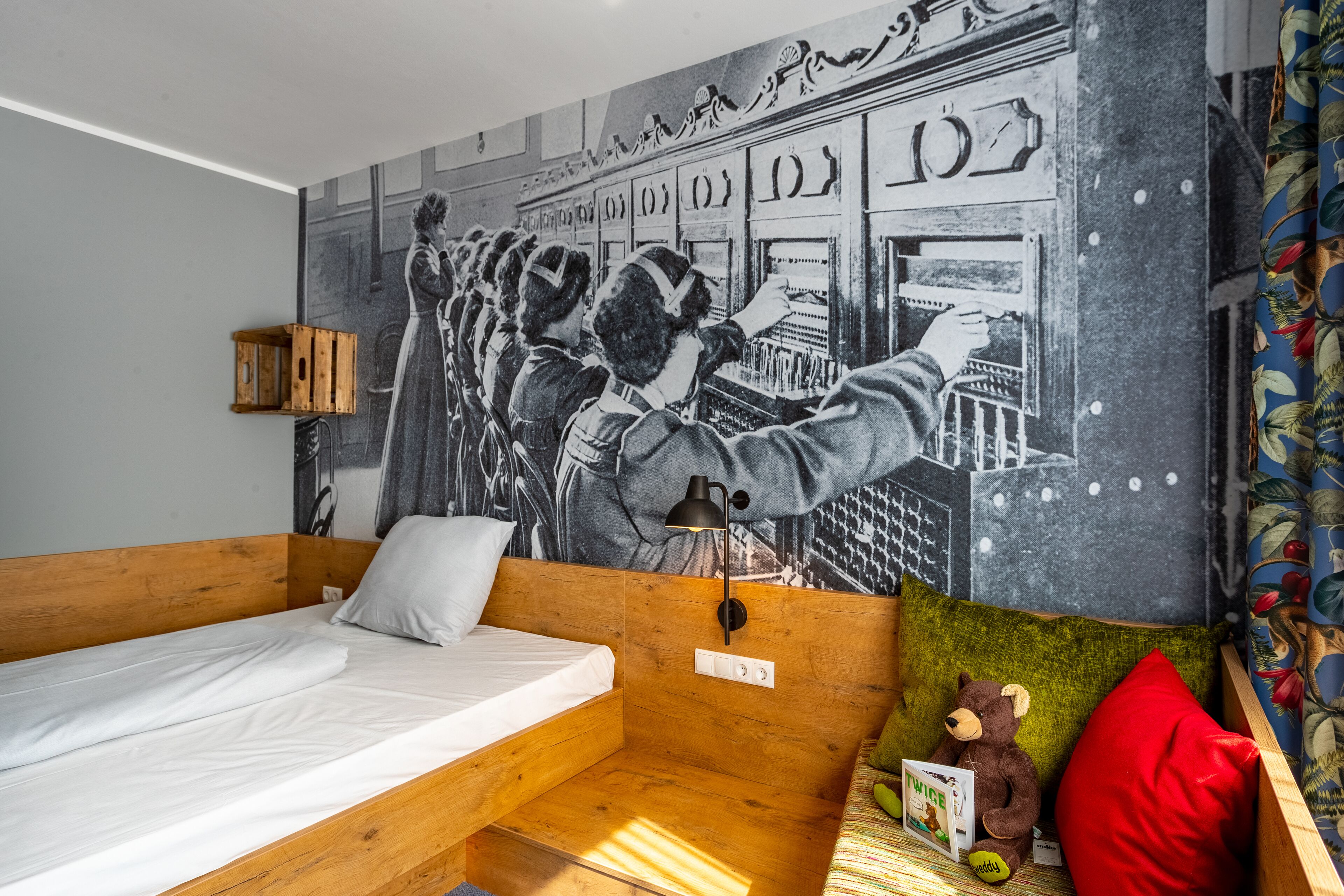 A room with a wooden bunk bed, a mural on the wall, a lamp, a teddy bear, and a pillow.