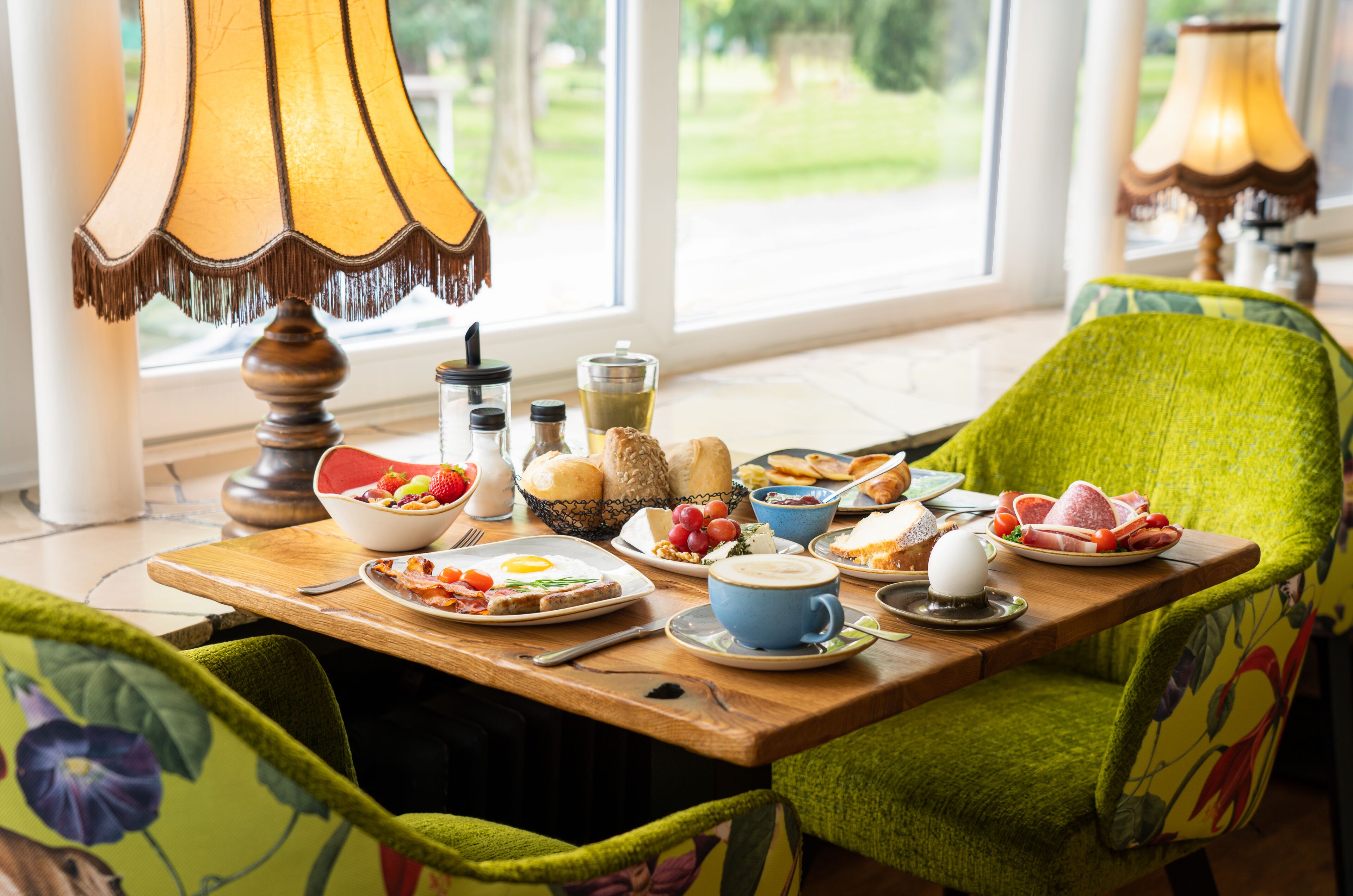 Una mesa de desayuno con diversos platos, una lámpara y sillas con tapicería floral.