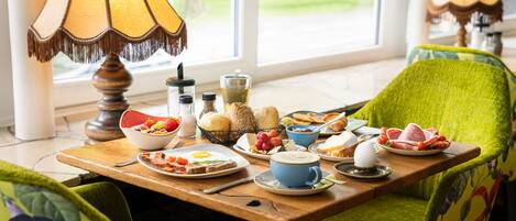 Una mesa de desayuno con diversos platos, una lámpara y sillas con tapicería floral.