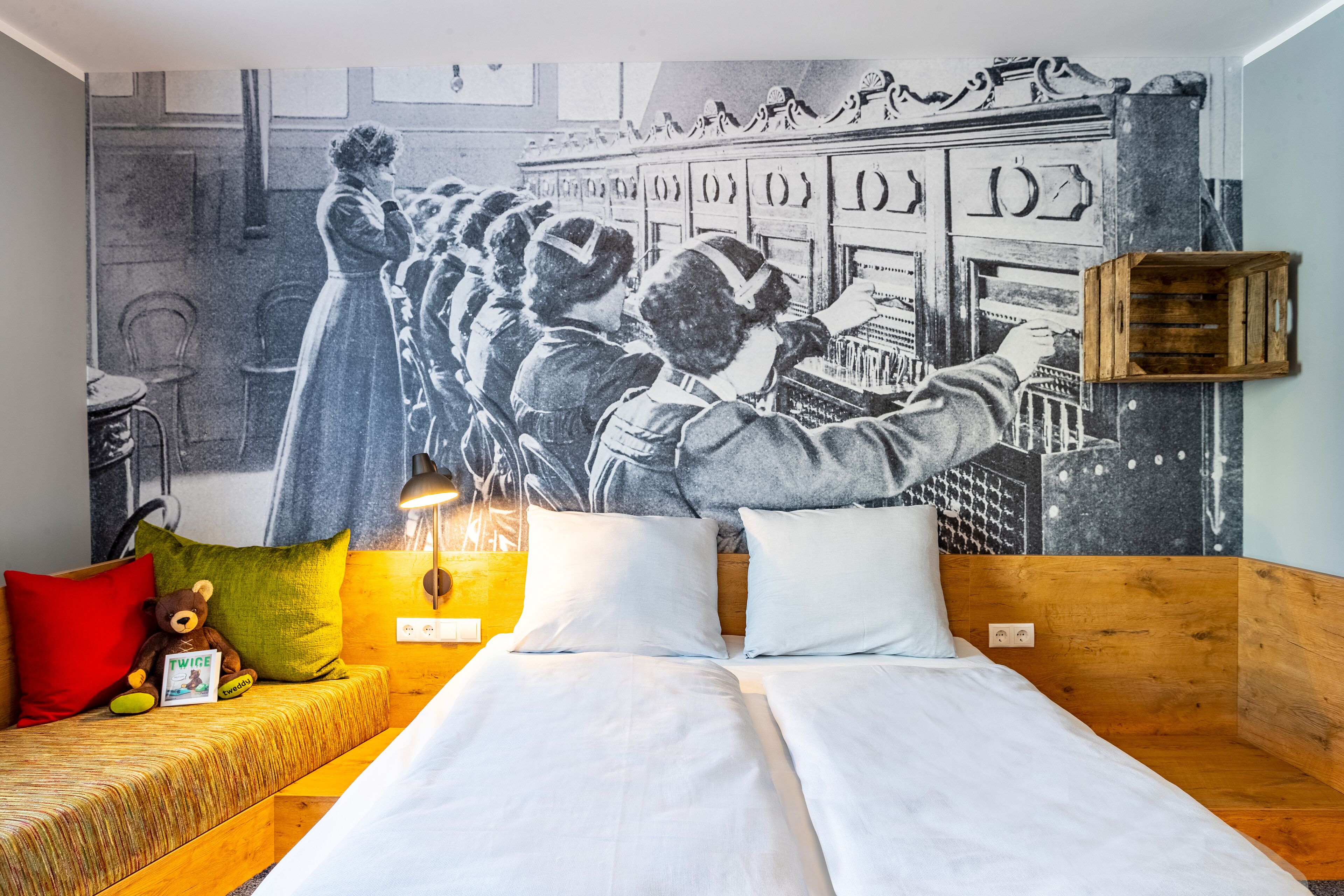 Une chambre avec un lit, une tête de lit en bois, une fresque murale et une petite caisse en bois.