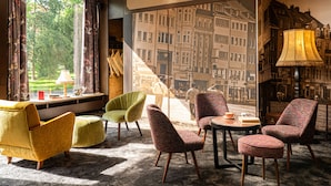A room with a large window, a view of a cityscape, and a variety of seating options including armchairs and a sofa. - tinyTwice Hotel Bonn (Bonn)