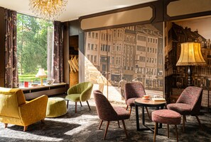 A room with a large window, a view of a cityscape, and a variety of seating options including armchairs and a sofa.