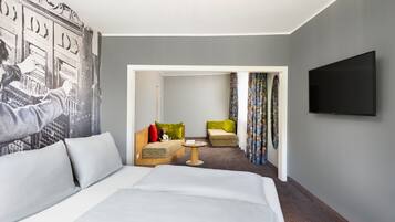 A hotel room with a bed, a TV, a seating area with chairs, and a colorful curtain.