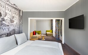 A hotel room with a bed, a TV, a seating area with chairs, and a colorful curtain. - tinyTwice Hotel Bonn (Bonn)