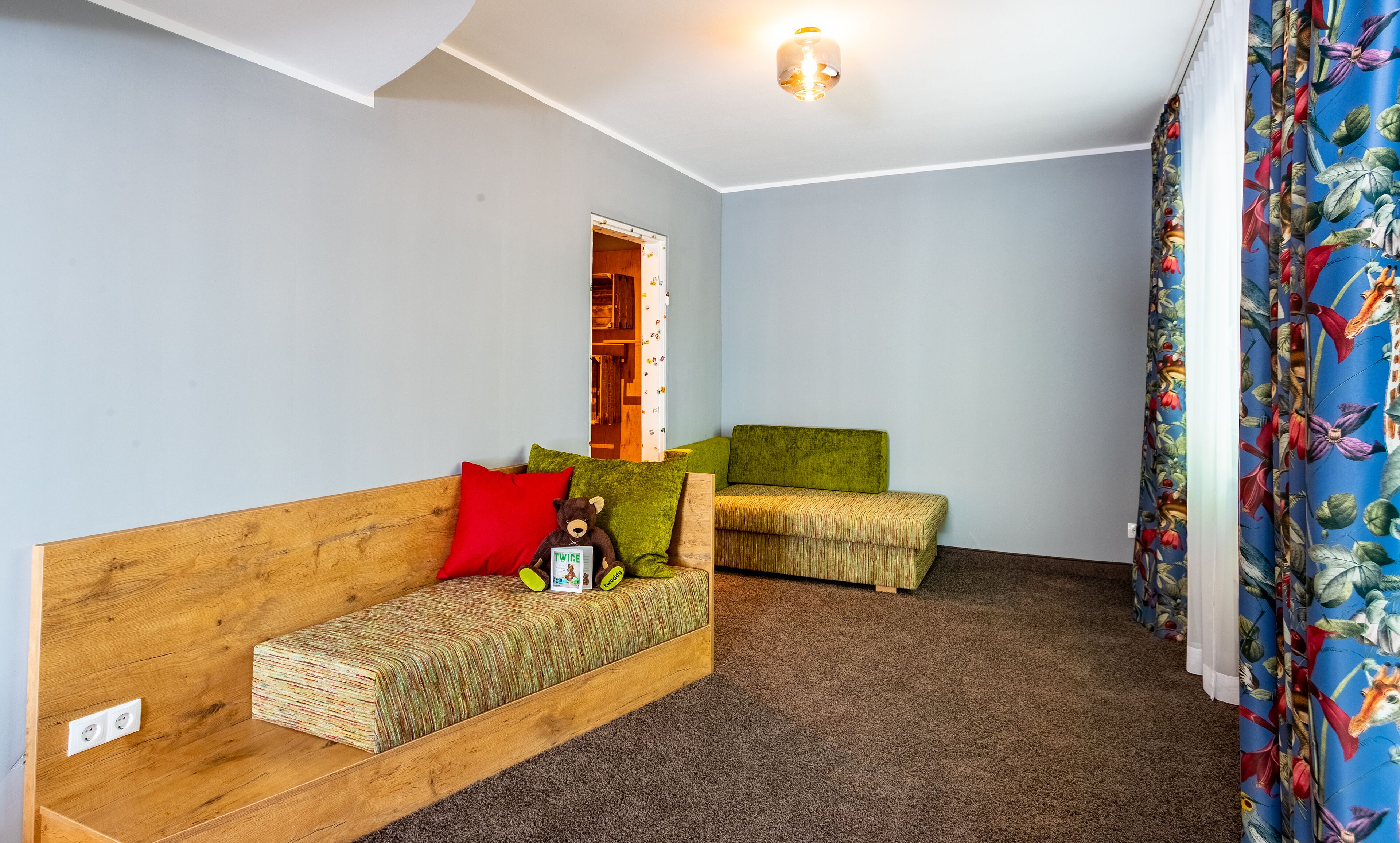 A small, cozy room with a wooden sofa, a green armchair, and a small table with a teddy bear and a card.
