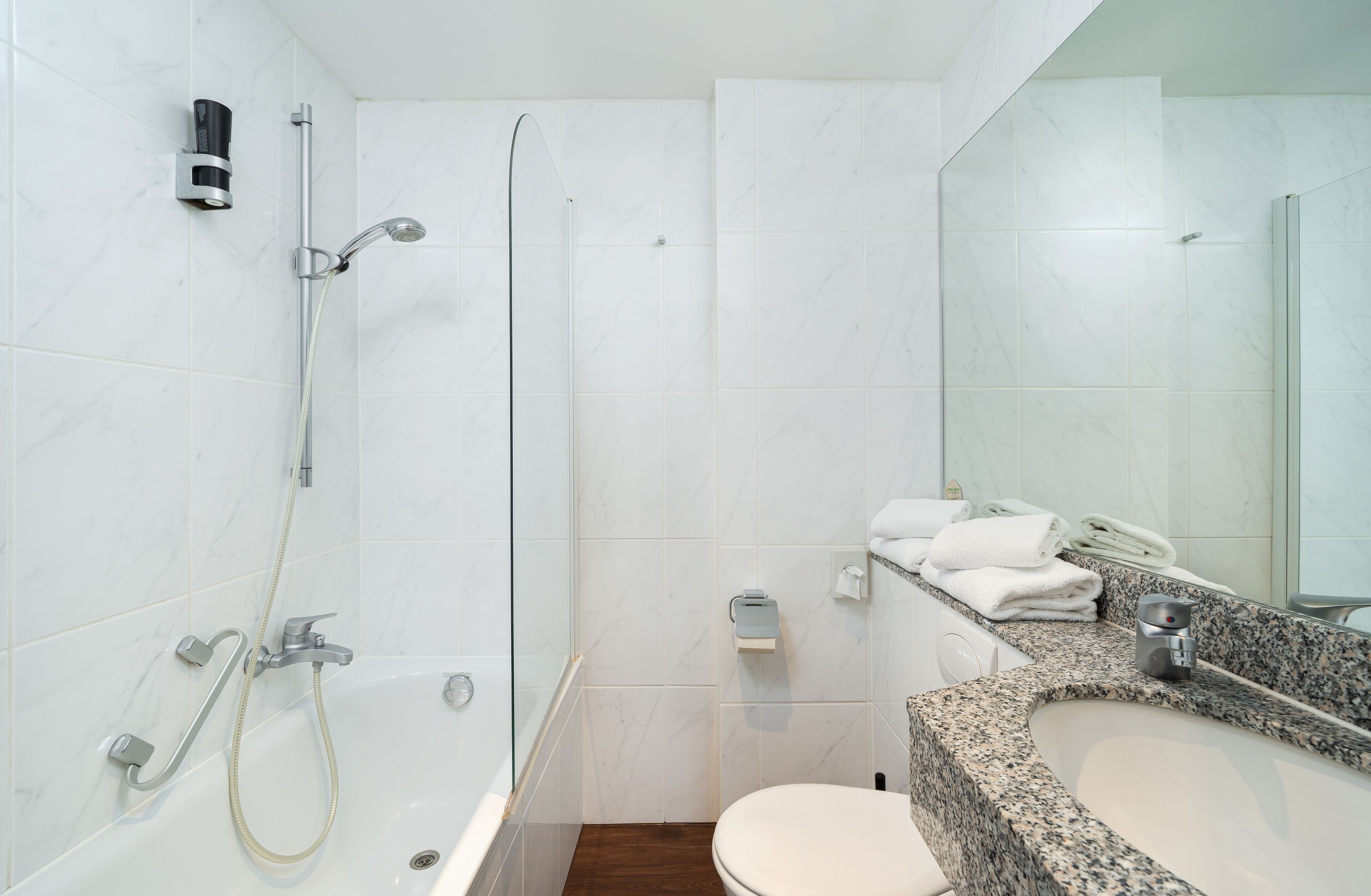 Ein modernes Badezimmer mit einer gläsernen Duschkabine, einem Waschtisch mit Granitplatte und einer weißen Toilette.