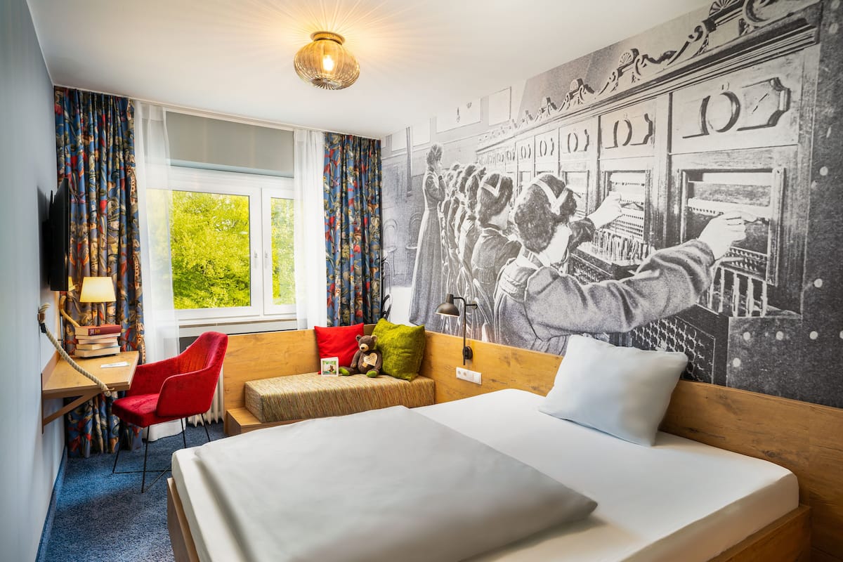 A hotel room with a bed, a desk, a chair, and a window with curtains.