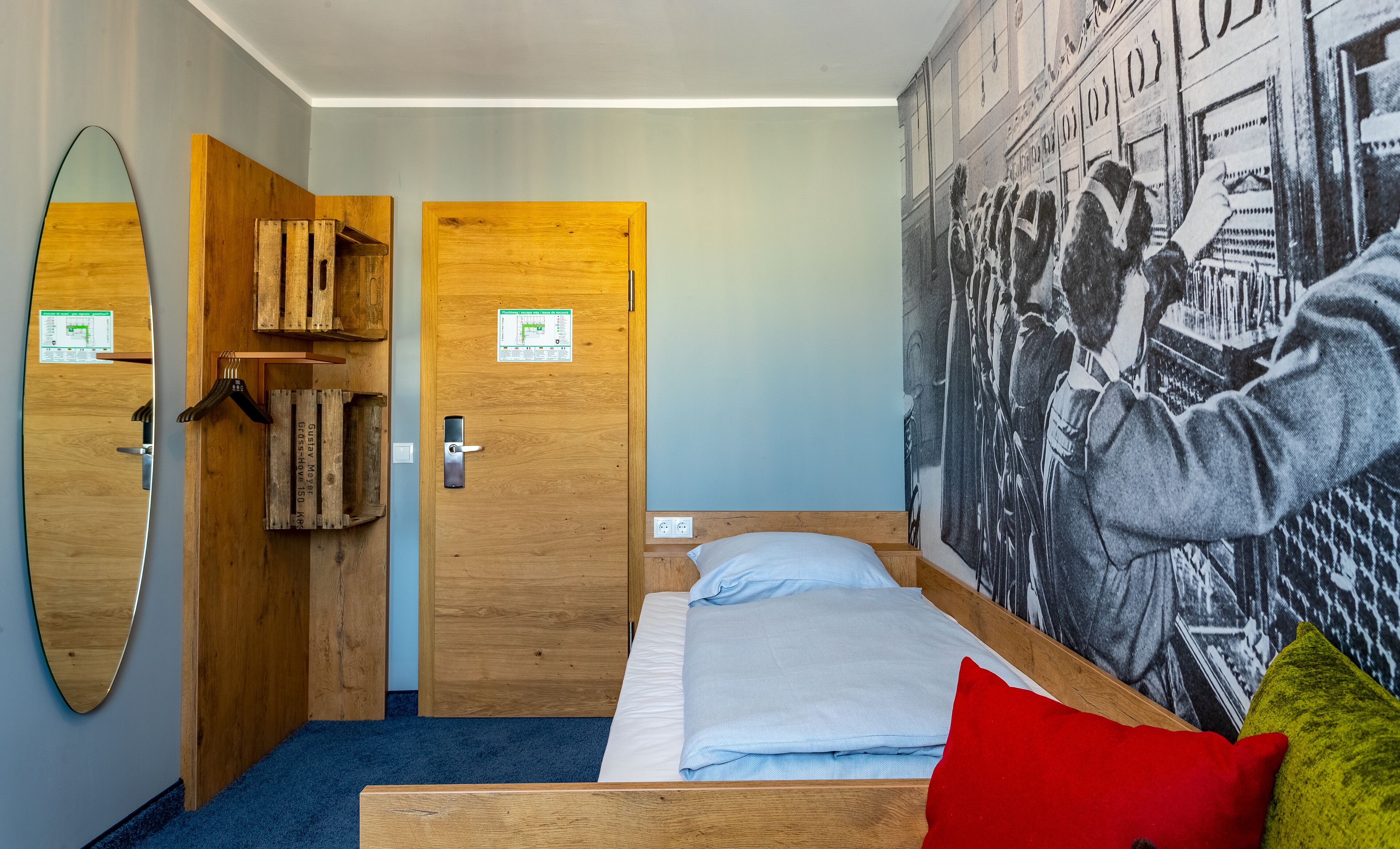 Ein Zimmer mit einem Bett, einem Holzschrank, einem Spiegel und einer Wand mit einem Schwarzweißfoto.