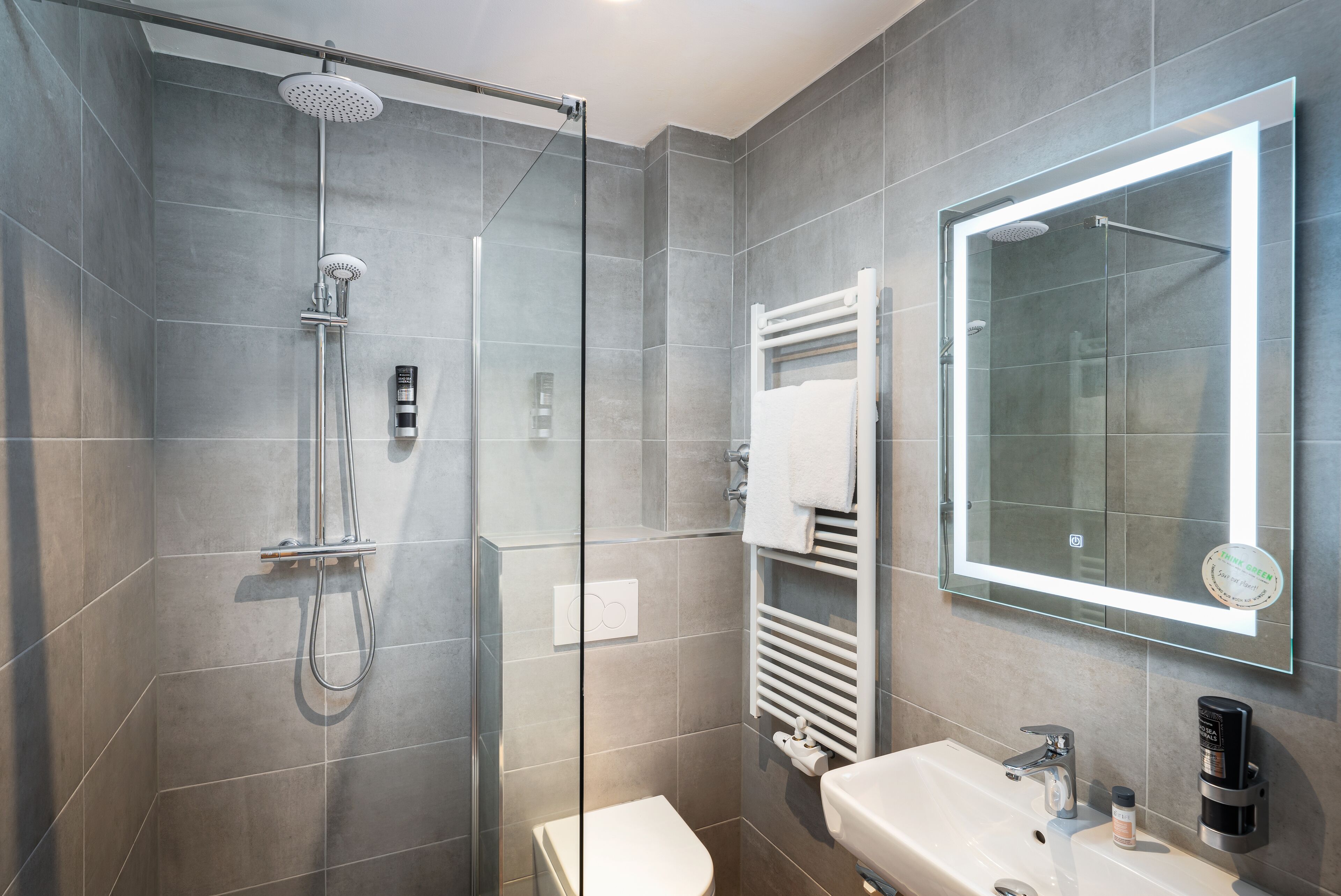 A modern bathroom with a glass-enclosed shower, a white sink, and a large mirror.