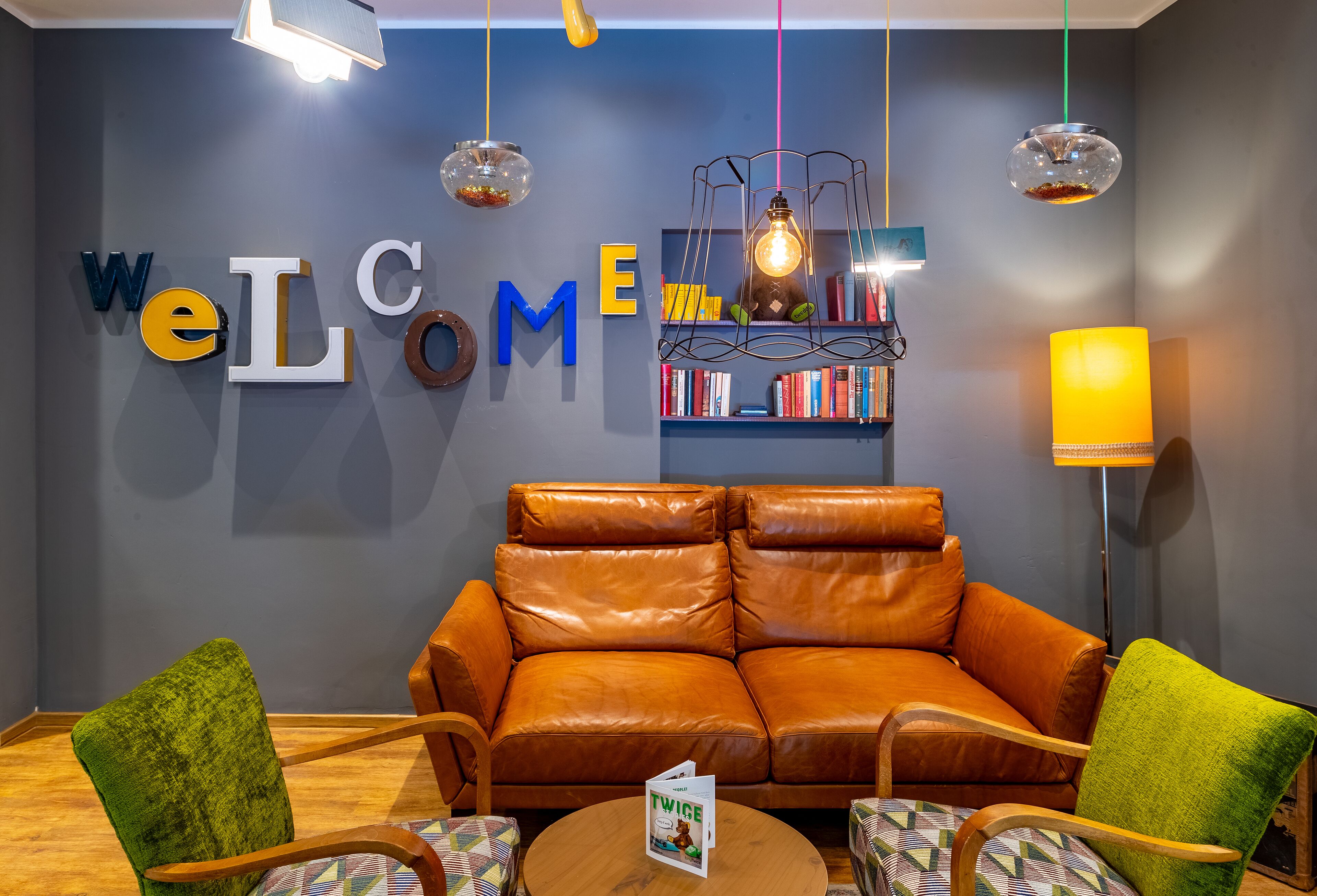 A modern living room with a leather sofa, green armchairs, a round coffee table, and a bookshelf.