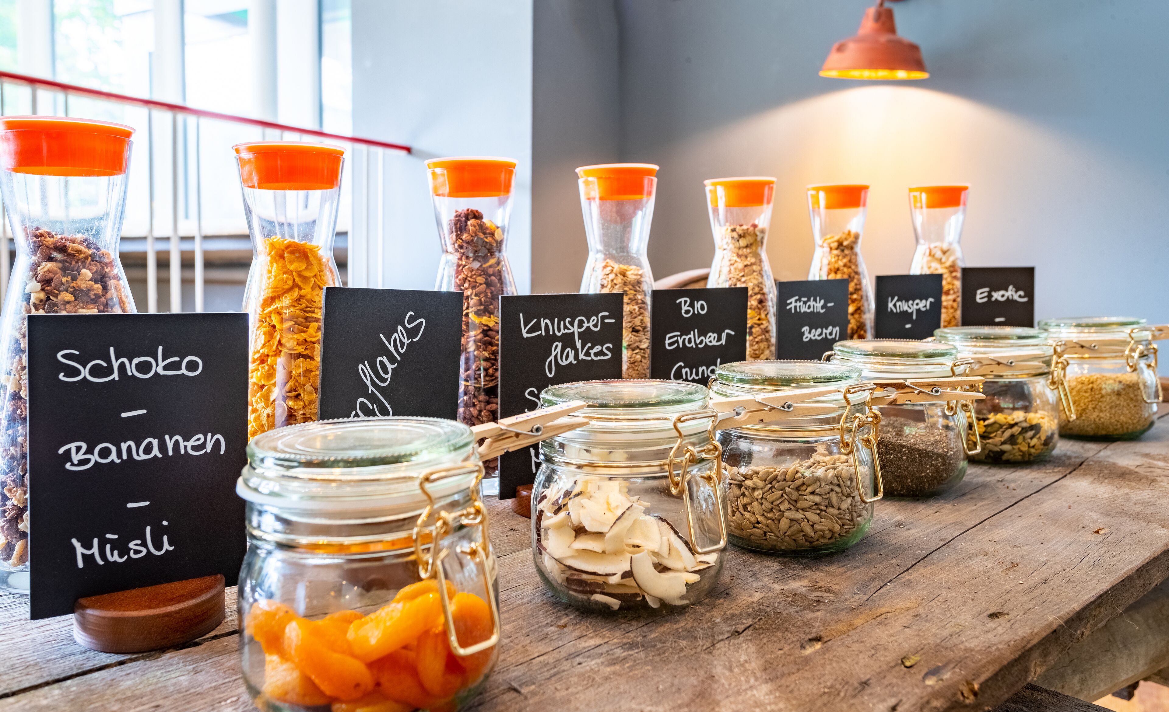 A variety of food items in glass jars with labels, displayed on a wooden table in a well-lit area.