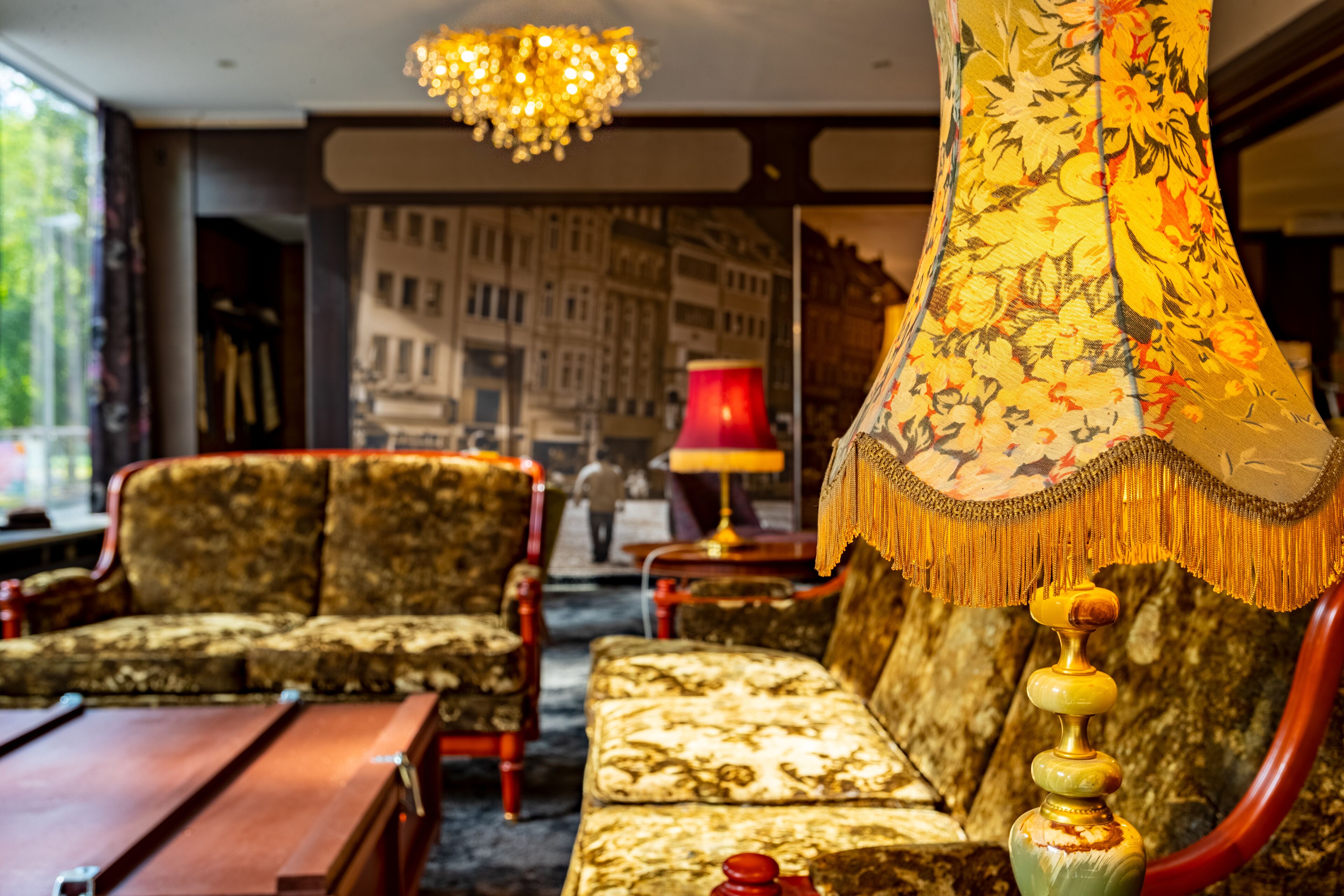 A room with a sofa, armchair, and a table. There is a lamp and a hanging lamp with a decorative shade.