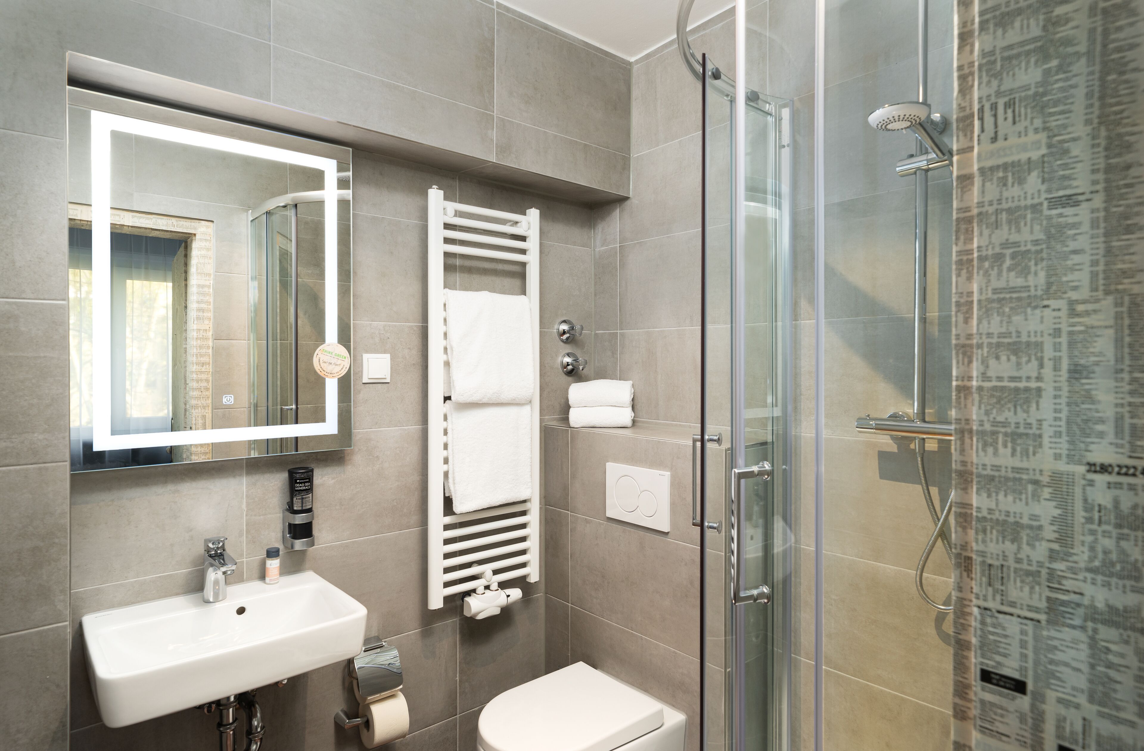 A modern bathroom with a glass shower enclosure, a white sink, and a towel rack.