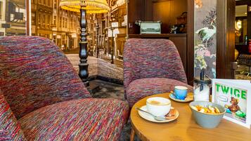 A cozy seating area with patterned upholstery, a table with a cup of coffee, a bowl of snacks, and a 'Twice Story' book.