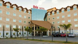 Een meerlaags hotel met een opvallend 'ibis HOTEL' bord, met een moderne glazen gevel en een traditioneel pannendak.