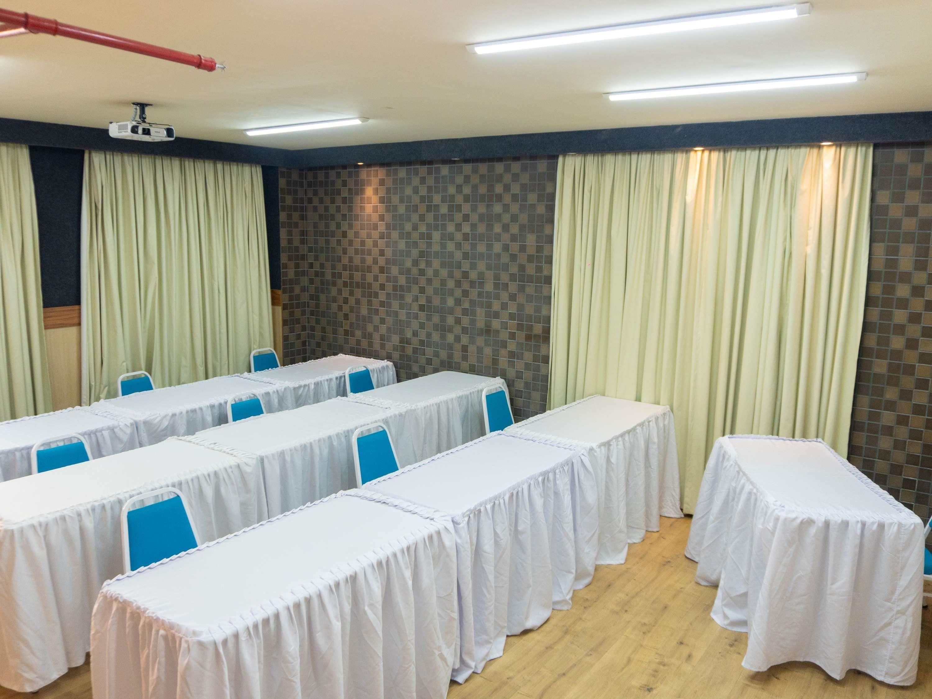 A conference room with tables covered in white tablecloths, blue chairs, a projector, and curtains.