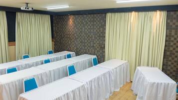 A conference room with tables covered in white tablecloths, blue chairs, a projector, and curtains.