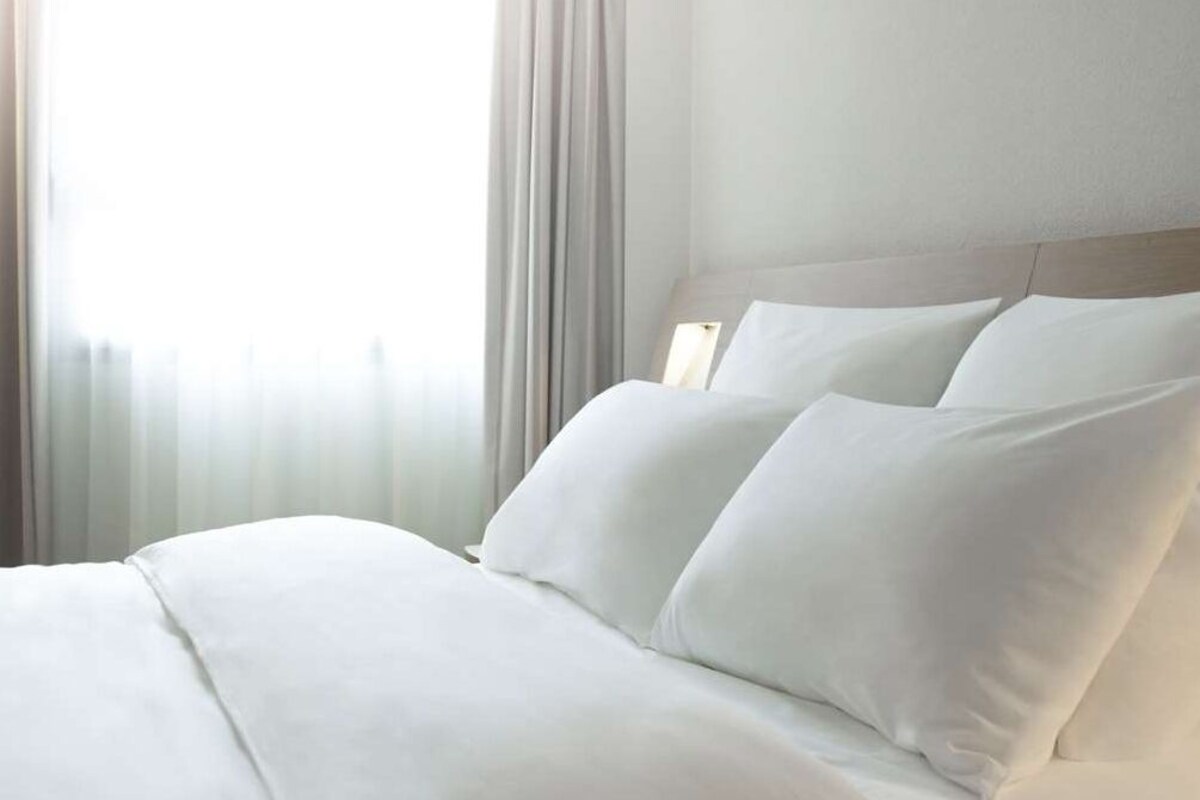 Een hotelkamer met een net opgemaakt bed, een hoofdeinde en een raam met gordijnen.